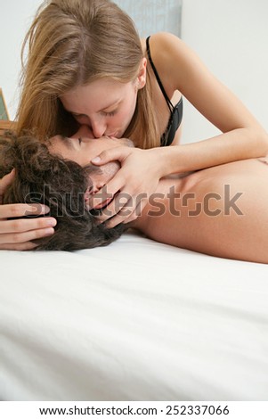 Close up portrait view of an attractive young couple kissing on the lips and hugging in hotel bed, indoors. Lovers couple and romance living lifestyle. Sensuality and relationships, home interior.