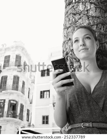Black and white close up portrait of a young professional tourist woman visiting a destination city, using a smartphone mobile phone on holiday. Travel and technology lifestyle and networking.