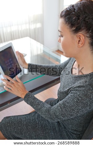 Side view of an attractive young businesswoman using a touch screen digital tablet to work at her work desk in an office space, interior. Professional business woman using technology, office indoors.