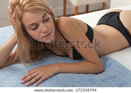 Beauty portrait of young woman relaxing on a luxury bed in a home bedroom, thoughtfully looking away, wearing sexy black bra lingerie, hotel room, indoors. Home living lifestyle skin care, interior.