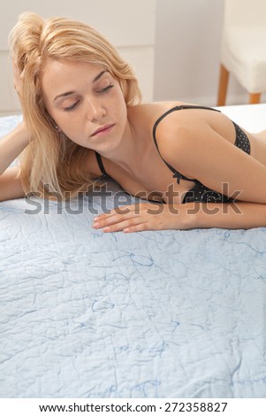 Beauty portrait of young woman relaxing on a luxury bed in a home bedroom, thoughtfully looking away, wearing sexy black bra lingerie, hotel room, indoors. Home living lifestyle skin care, interior.