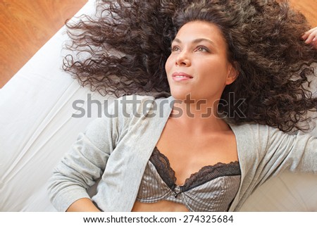 Overhead portrait of a beautiful young exotic woman relaxing on a bed at home, wearing sexy lingerie, interior space. Healthy wellness and well being living aspirational lifestyle, bedroom indoors.