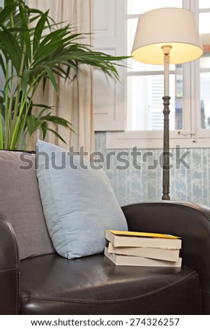 Still life interior relaxing home reading room with quality leather armchair in a stylish house. Aspirational and relaxing room with books, cushions and a lamp by a window, indoors living lifestyle.