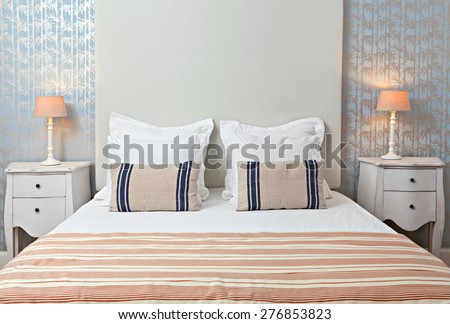 Still life home interior view of double bed bedroom stylish home with comfortable cushions and pillows. Design hotel room with a pattern wallpaper and elegant furnishings, aspirational lifestyle.