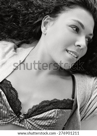 Black and white portrait of beautiful young exotic woman laying relaxing on bed at home, smiling wearing sexy lingerie, interior space. Well being home living aspirational lifestyle, bedroom indoors.