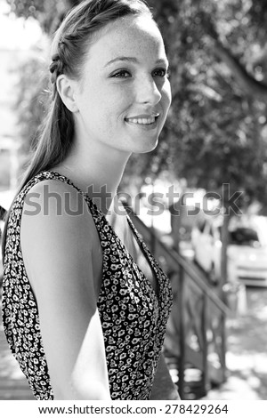 Black and white beauty portrait of a young attractive tourist woman on holiday, smiling, exterior. Travel and lifestyle on a sunny summer vacation break, outdoors park. Beautiful woman with freckles.