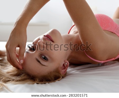 Over head beauty portrait of a young beautiful sexy woman laying on a bed at home in pink lingerie, flirting and looking at the camera in a bedroom, interior. Health aspirational lifestyle, indoors.