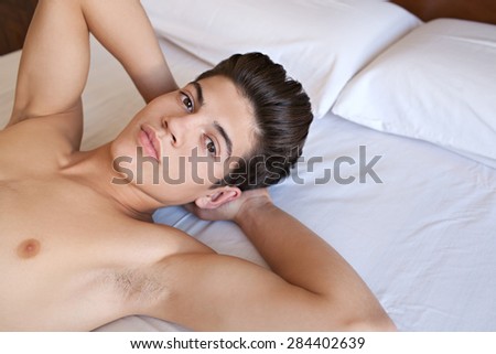 Close up beauty portrait of a young adolescent teenager man laying on a bed at home with a bare chest, thoughtful indoors. Male puberty and growing up issues. Interior beauty and healthy living.