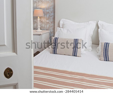 Still life of a luxury home bedroom in a quality family home, seen through a door ajar, semi open bedroom door, interior. Aspirational bed in home room with a bamboo pattern wallpaper indoors.