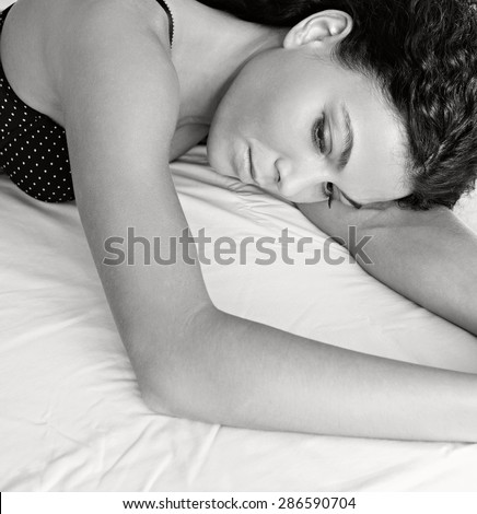 Black and white beauty portrait of a young beautiful exotic sexy woman laying on a bed at home in black lingerie, relaxing in a bedroom, interior. Health well being aspirational lifestyle, indoors.