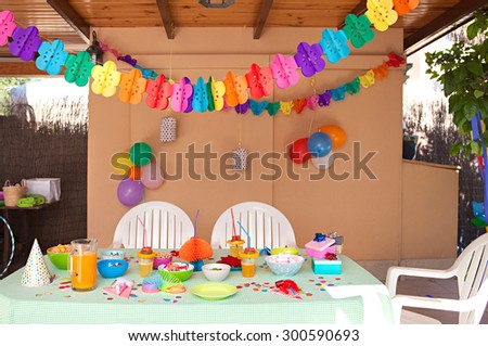 Still life view of a children birthday party table decorated with fun and colorful deco and balloons in a home garden space, outdoors. Kids party decorations and fun activities space, home exterior.