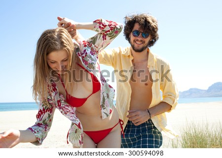 Attractive young couple dancing together on a beach on a summer holiday having fun and being active with a blue sea and sky, outdoors coast. Travel recreational lifestyle, exterior space.