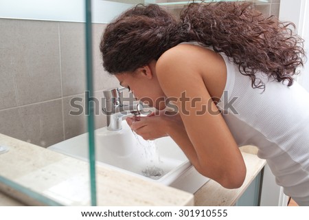 Side view of a beautiful young woman washing her face splashing water in a home bathroom sink, home interior. Wellness, well being and healthy skin care lifestyle. Girl grooming indoors, routine.