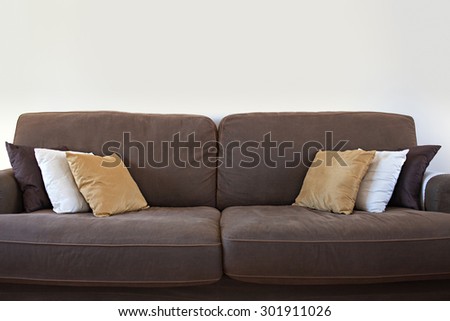 Still life view of a family home living room with a comfortable brown sofa with cushions against a white wall, house interior. Home relaxing and lounging empty space, indoors.
