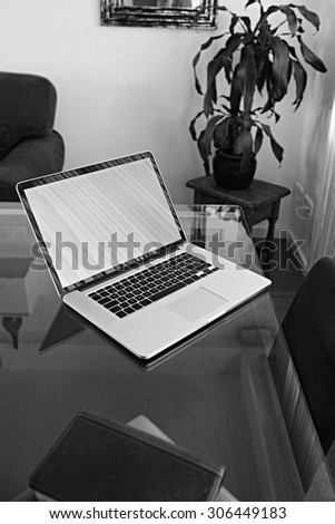 Black and white still life of a home office living room with open laptop computer on a glass desk, professional office interior with paperwork. Working from home desk workplace, technology indoors.