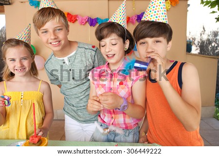 Portrait of group of four children friends enjoying a birthday party celebrating wearing party hats in a home garden, outdoors. Colorful kids having fun together smiling at the camera, home exterior.