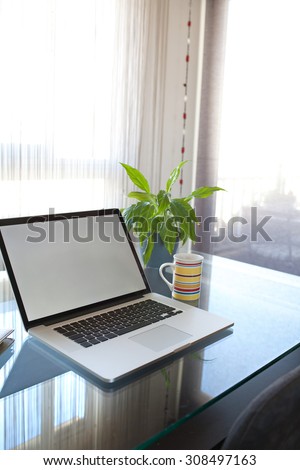 Still life of a living room in a city apartment with an open laptop on a professional glass desk workplace by a bright window, interior. Home office technology, indoors. Working from home lifestyle.