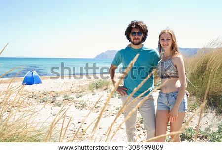 Tourist couple smiling together on a beach with clear waters and sand dunes, enjoying a camping holiday, beach exterior. Travel and lifestyle couple enjoying a romantic vacation, nature exterior.