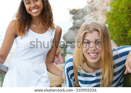 Beauty portrait of two young teenager girls of different ethnic origins friends laughing together by the sea on a summer holiday, outdoors. Travel fun and adolescent lifestyle, nature beach exterior.