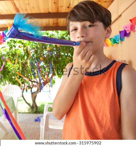 Portrait of cute child boy playing with a colorful party blower in a sunny summer birthday party in a home garden, outdoors. Kid having fun and smiling on a summer holiday, home exterior.