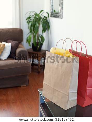 Still life of paper shopping bags in a stylish living room, home interior. Carrier bags on a table in a room with wooden floor in elegant room with sofa, indoors. Indulgence and consumerism lifestyle.