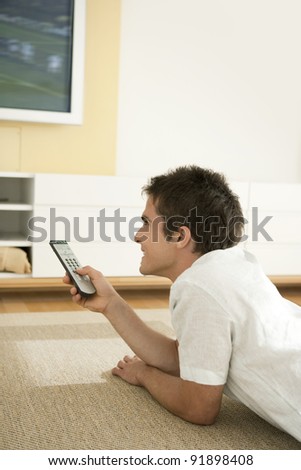Young professional using a tv remote control while watching a flat screen tv at home.