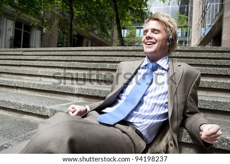 Young businessman listening to music with headphones while sitting down on some steps in the city.