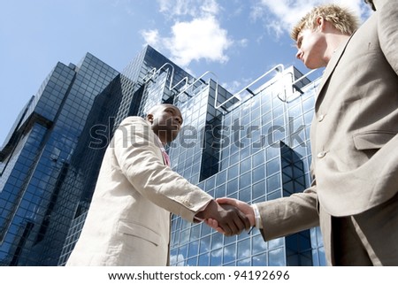 Two businessmen shaking hands in front of a glass modern building in the city.