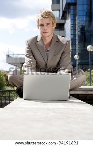 Businessman sitting down by an office building, using his laptop.