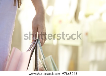 Detail close up of a woman\'s hand holding shopping bags by fashion store.