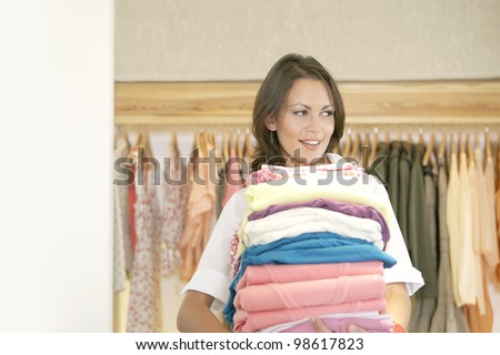 Shop assistant holding a pile of clothes in a fashion store