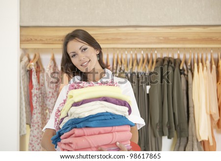 Shop assistant holding a pile of clothes in a fashion store