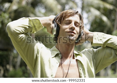 Happy man listening to music with headphones in a tropical garden.