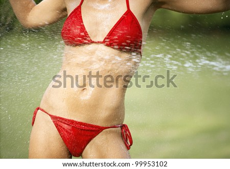 Water being sprayed onto a young woman\'s body wearing a red bikini, outdoors.