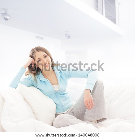 Beautiful and happy young woman sitting on the sofa over the domestic background