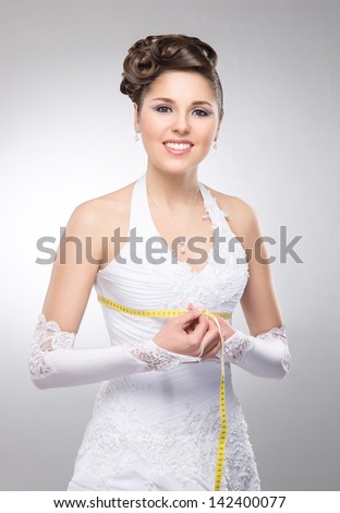 Young and beautiful bride measures her waist over the grey background