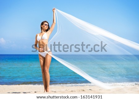 A beautiful woman in a swimsuit posing with a silk blanket on the beach