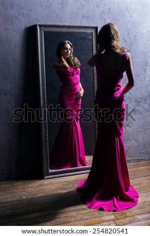 Young and gorgeous actress in a long dress preparing in a dressing room in front of a mirror.