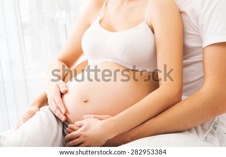 Close-up picture of man and woman awaiting a baby. Male hands on a pregnant belly.