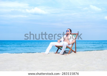 Young, fit and handsome man with athletic and muscled body chilling in a beach chair at summer