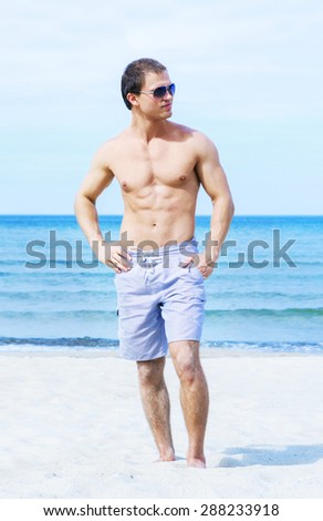 Young, fit and handsome man with athletic and muscled body walking on a summer beach