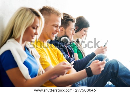 Group of students on a break. Focus on a boy using smartphone. Background is blurry.
