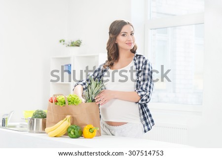 Beautiful pregnant woman in the kitchen with shopping bag and pineapple.