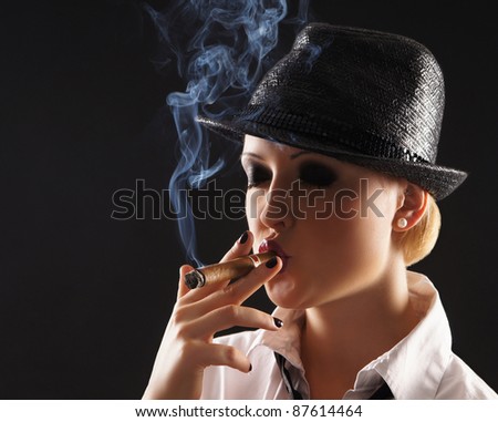 Young attractive female gangster smoking cigar over dark background