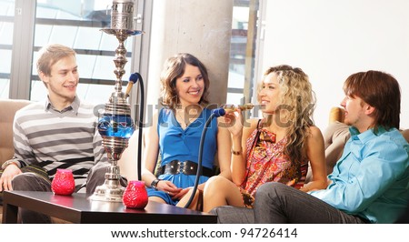Group of young and sexy people smoking hookah in the lounge cafe
