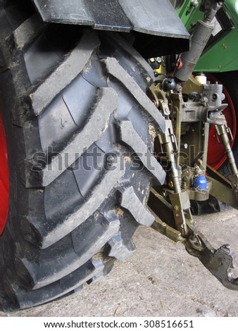 Row of deep tractor tire prints in the sand. Close up of industrial vehicle heavy black rubber tire, bright red metal wheel.