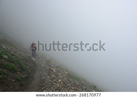 male hiker with a backpack on a highland alpine trail in heavy fog, view from the back
