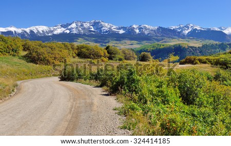 road through mountains with colorful yellow, green and red aspen during foliage season on Last Dollar road in Colorado
