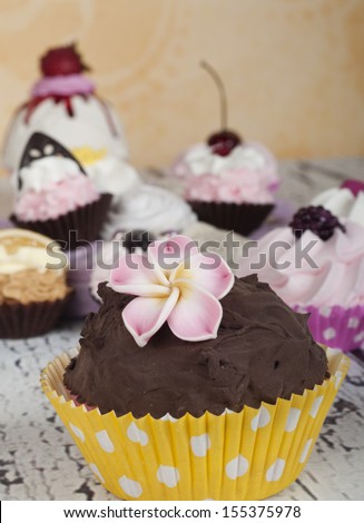 chocolate cupcake with pink flower and lots of cupcakes in the background
