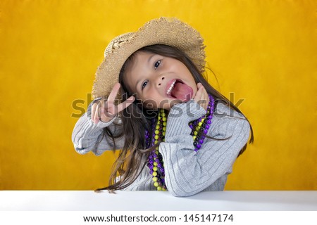 Cute little girl with hat, gray sweater and necklaces sticking his tongue out while doing the victory sign with his hand